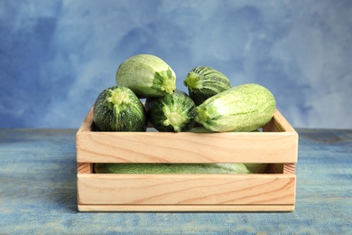 Photo of Wooden crate with fresh ripe green zucchinis on table against blue background