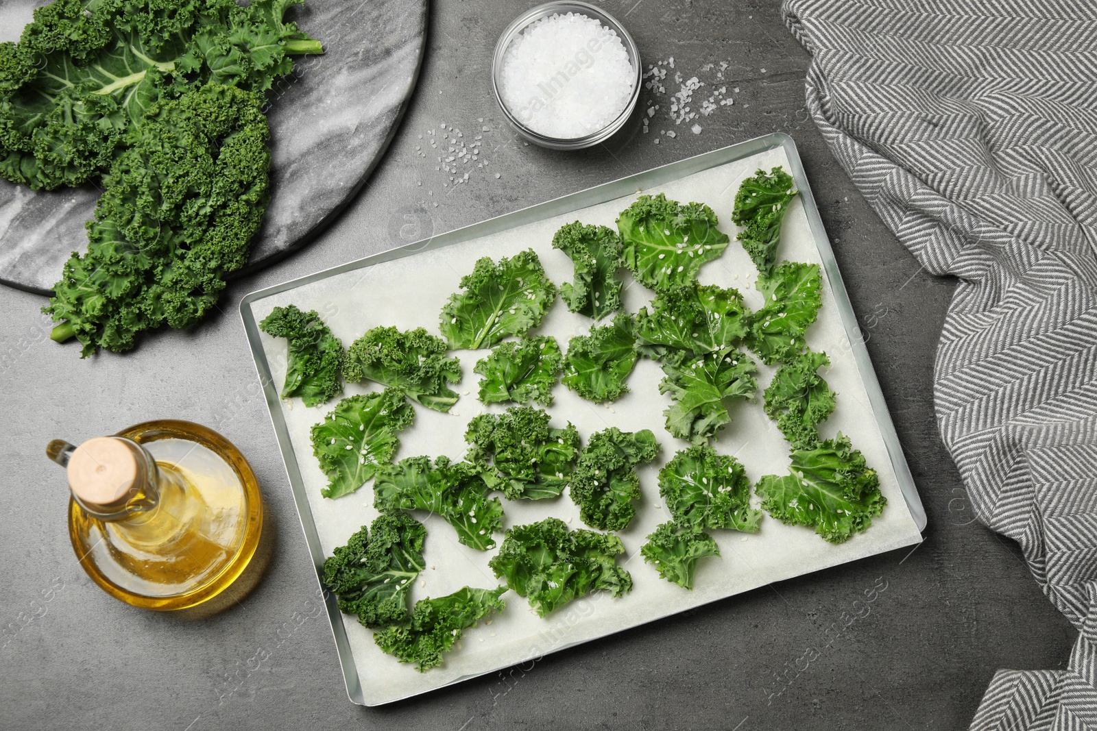 Photo of Raw cabbage leaves with seeds on grey table, flat lay. Preparing kale chips