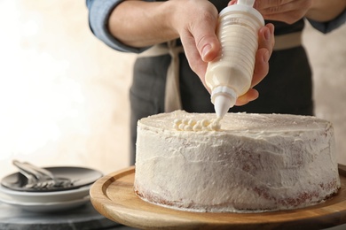 Woman decorating delicious cake with fresh cream at table indoors, closeup. Homemade pastry