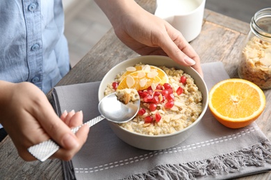 Photo of Woman eating quinoa porridge with nuts, orange and pomegranate seeds at table, closeup. Tasty breakfast