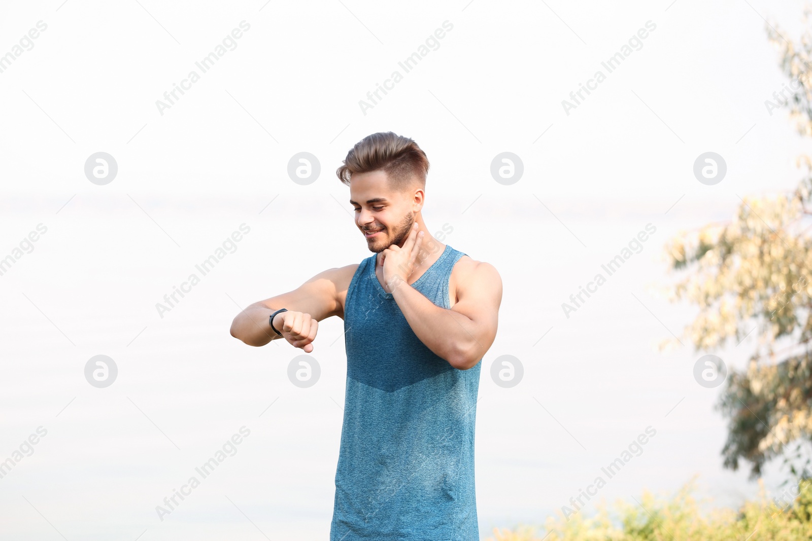 Photo of Young man checking pulse outdoors on sunny day