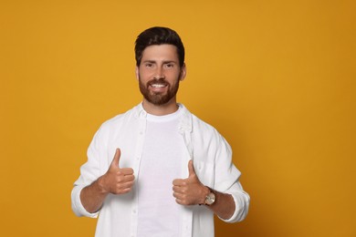 Photo of Handsome bearded man showing thumbs up on orange background. Space for text
