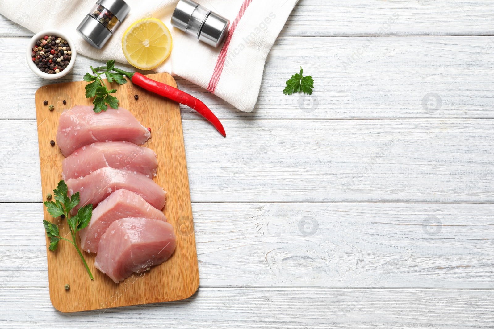 Photo of Board with cut raw turkey fillet and ingredients on white wooden background, top view. Space for text