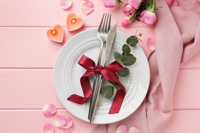 Place setting with heart shaped candles and bouquet of roses on pink wooden table, flat lay. Romantic dinner