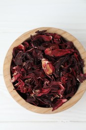 Hibiscus tea. Bowl with dried roselle calyces on white wooden table, top view
