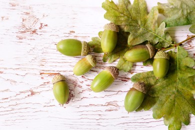 Green acorns and oak leaves on white wooden table, flat lay. Space for text