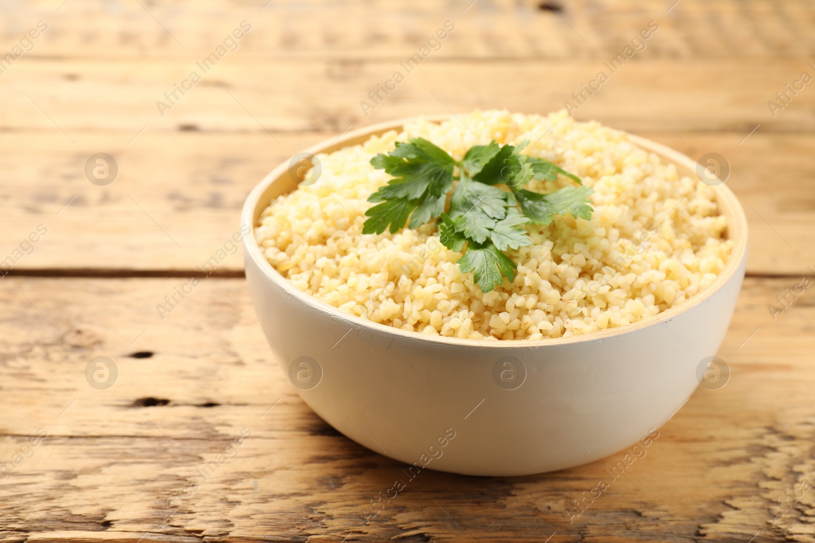 Photo of Delicious bulgur with parsley on wooden table, closeup. Space for text