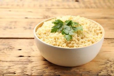 Photo of Delicious bulgur with parsley on wooden table, closeup. Space for text