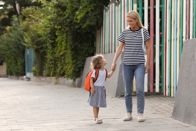 Photo of Happy woman and her little daughter on their way to kindergarten outdoors. Space for text
