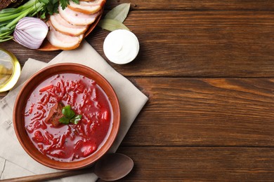 Photo of Stylish brown clay bowl with Ukrainian borsch served on wooden table, flat lay. Space for text
