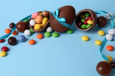 Tasty chocolate eggs and different candies on light blue background, space for text