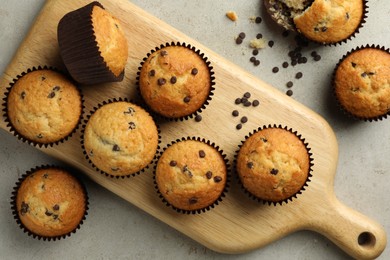 Photo of Delicious sweet muffins with chocolate chips on grey textured table, flat lay