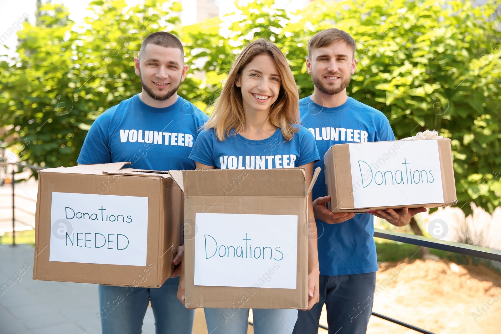 Photo of Young volunteers holding boxes with donations for poor people outdoors