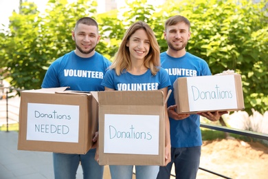 Young volunteers holding boxes with donations for poor people outdoors