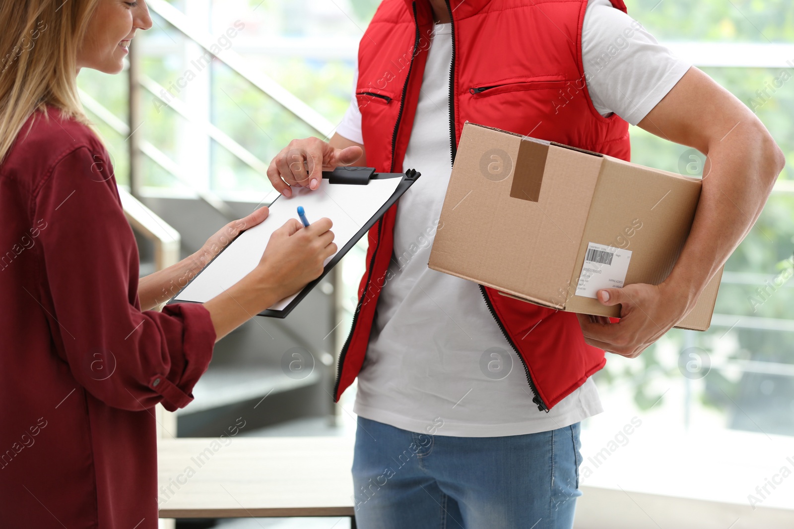 Photo of Young woman signing papers for delivered parcel indoors. Courier service