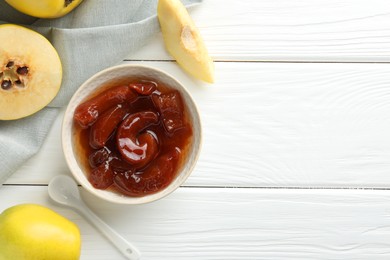 Tasty homemade quince jam in bowl, spoon and fruits on white wooden table, flat lay. Space for text