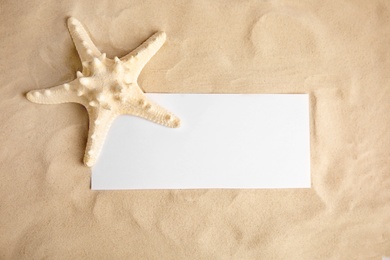 Photo of Beautiful starfish and blank card on sand, top view. Space for text