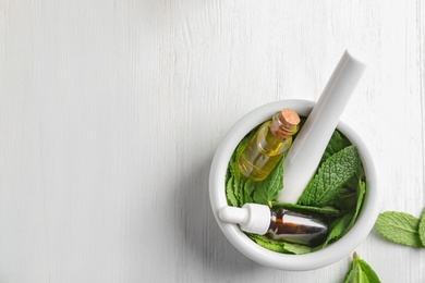 Mortar with bottles of essential oil and mint leaves on white wooden background