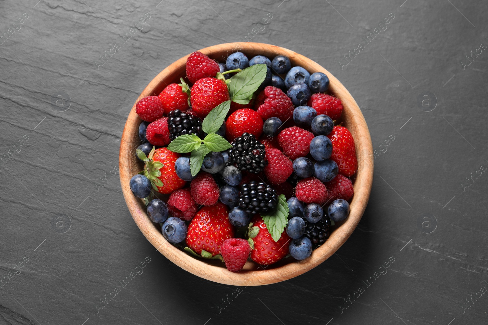 Photo of Many different fresh ripe berries in wooden bowl on black table, top view