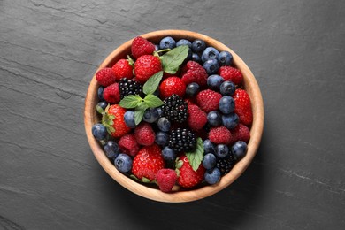 Many different fresh ripe berries in wooden bowl on black table, top view