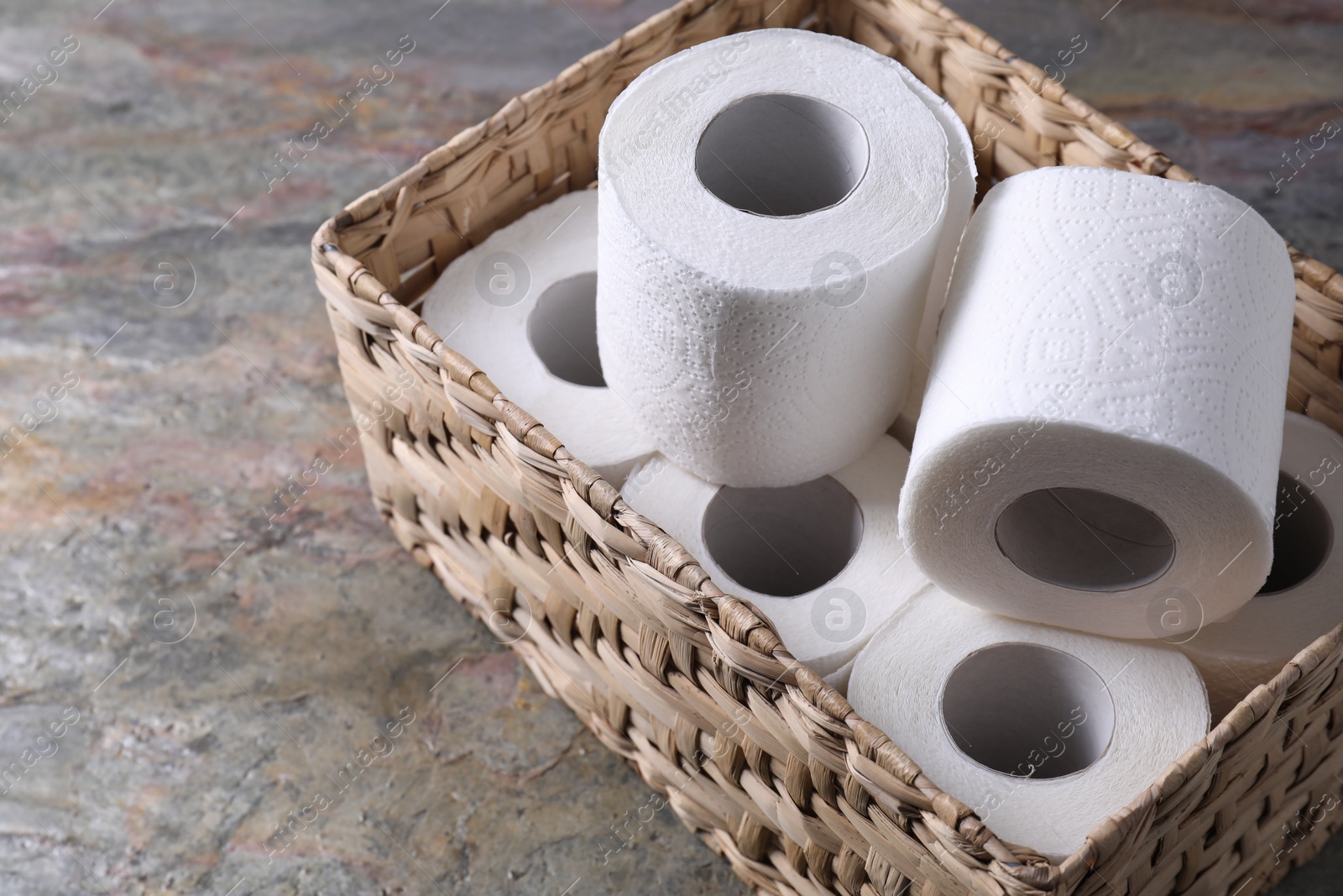 Photo of Toilet paper rolls in wicker basket on textured table, space for text