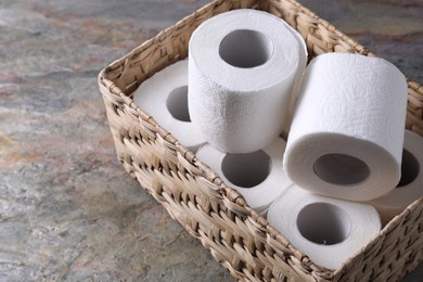Toilet paper rolls in wicker basket on textured table, space for text