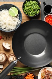 Photo of Black wok, spices and products on dark table, flat lay