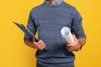 Photo of Professional engineer with clipboard and draft on yellow background, closeup