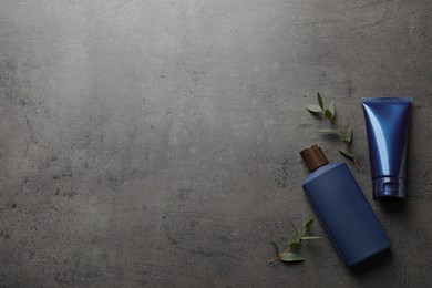Men's facial cream, shampoo and green leaves on grey stone table, flat lay. Mockup for design