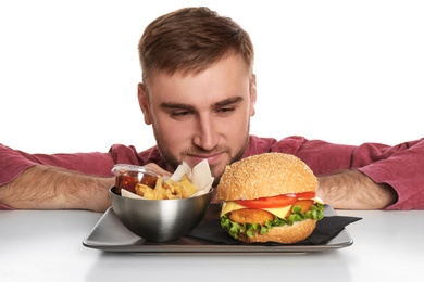 Photo of Young man and plate with French fries and tasty burger on white background