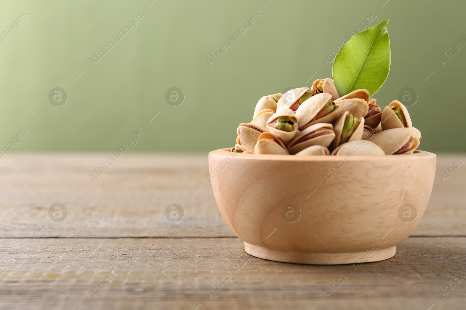 Photo of Tasty pistachios in bowl on wooden table against olive background, closeup. Space for text