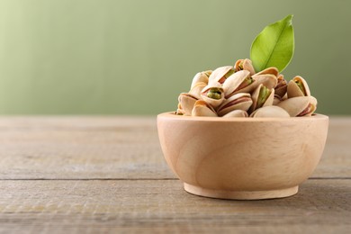 Photo of Tasty pistachios in bowl on wooden table against olive background, closeup. Space for text