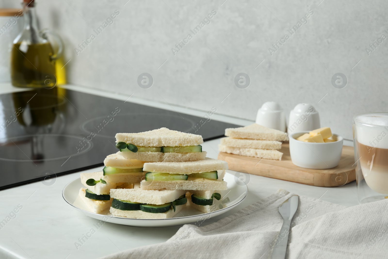 Photo of Tasty sandwiches with cucumber, butter and microgreens on white table in kitchen