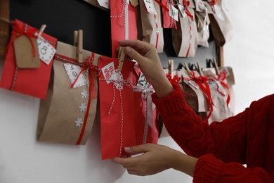 Woman hanging paper bag with gift on white wall, closeup. Christmas advent calendar