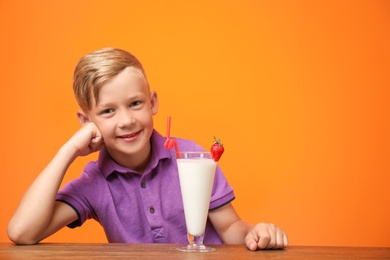 Photo of Little boy with glass of milk shake at table on color background