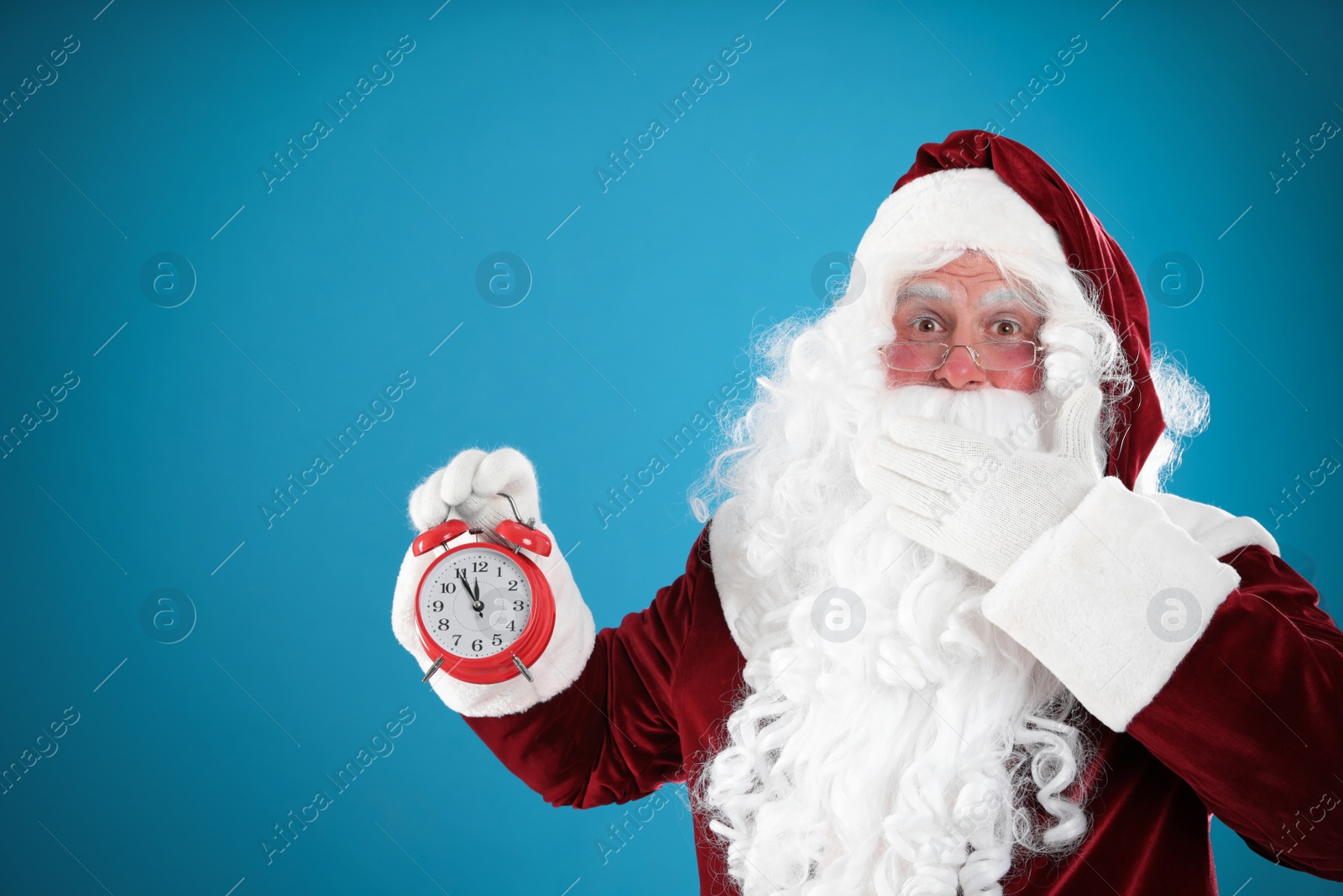 Photo of Santa Claus holding alarm clock on blue background, space for text. Christmas countdown