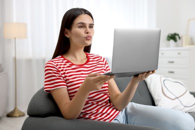 Photo of Young woman having video chat via laptop and blowing kiss on sofa in room