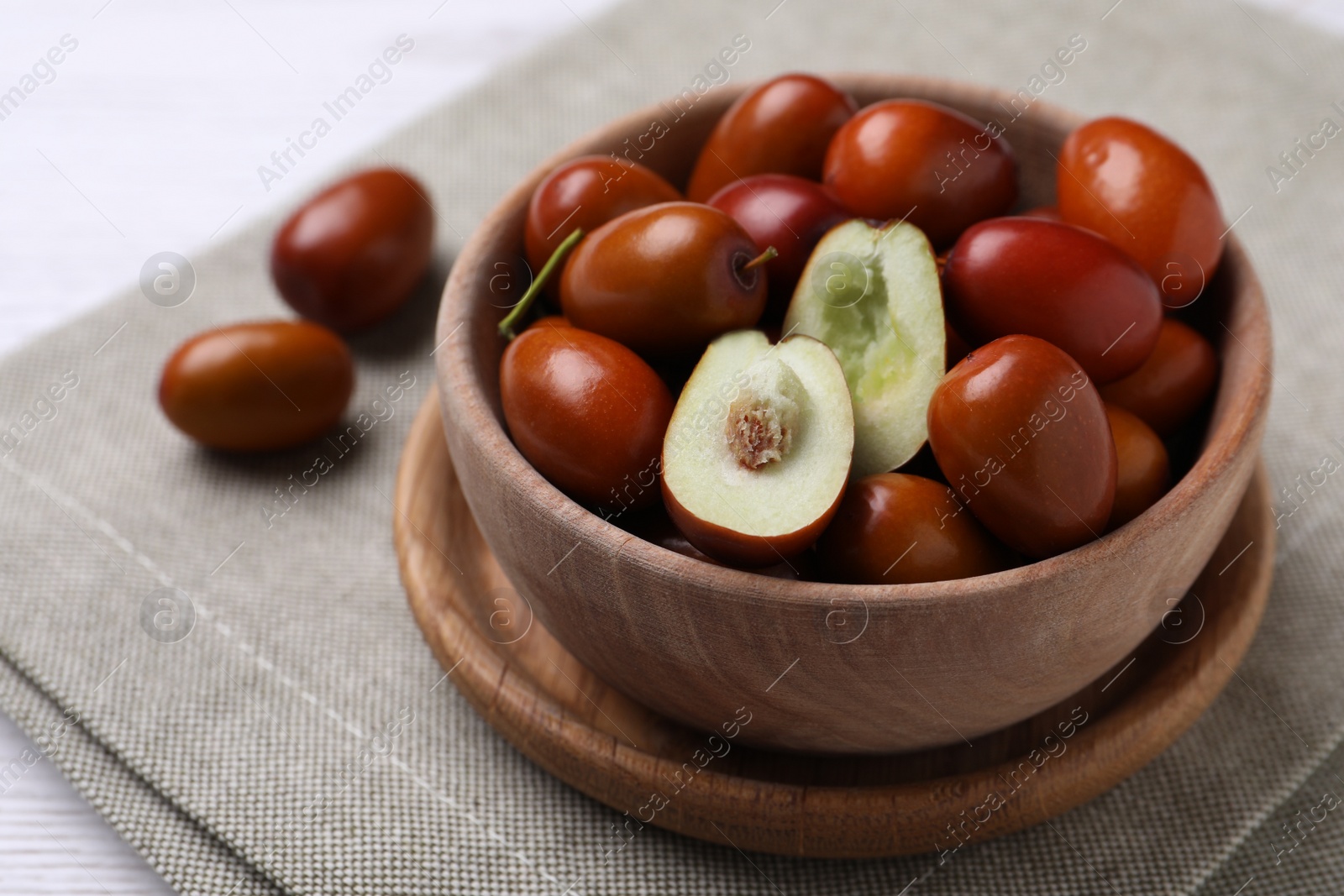 Photo of Fresh Ziziphus jujuba fruits in wooden bowl on table, closeup