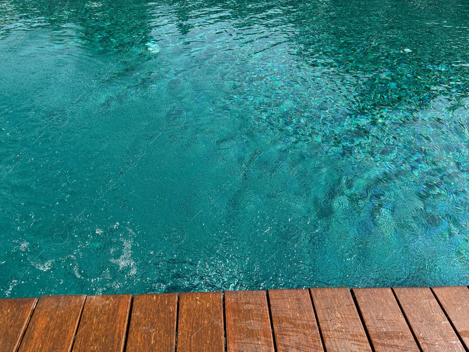 Photo of Clear rippled water in swimming pool and wooden deck outdoors. Space for text