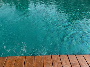 Photo of Clear rippled water in swimming pool and wooden deck outdoors. Space for text