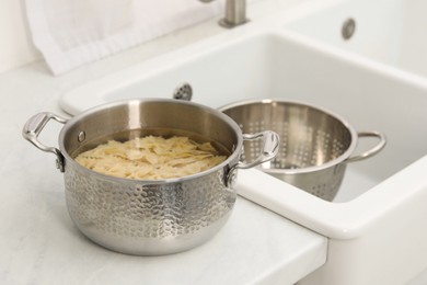 Cooked pasta in metal pot on countertop near sink