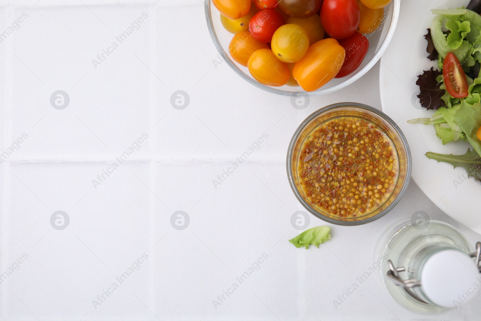 Photo of Tasty vinaigrette sauce in glass, vinegar, tomatoes and salad on light tiled table, flat lay. Space for text