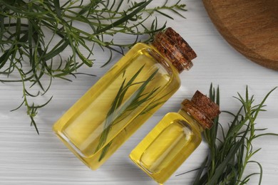 Photo of Bottles of essential oil and fresh tarragon sprigs on white wooden table, flat lay