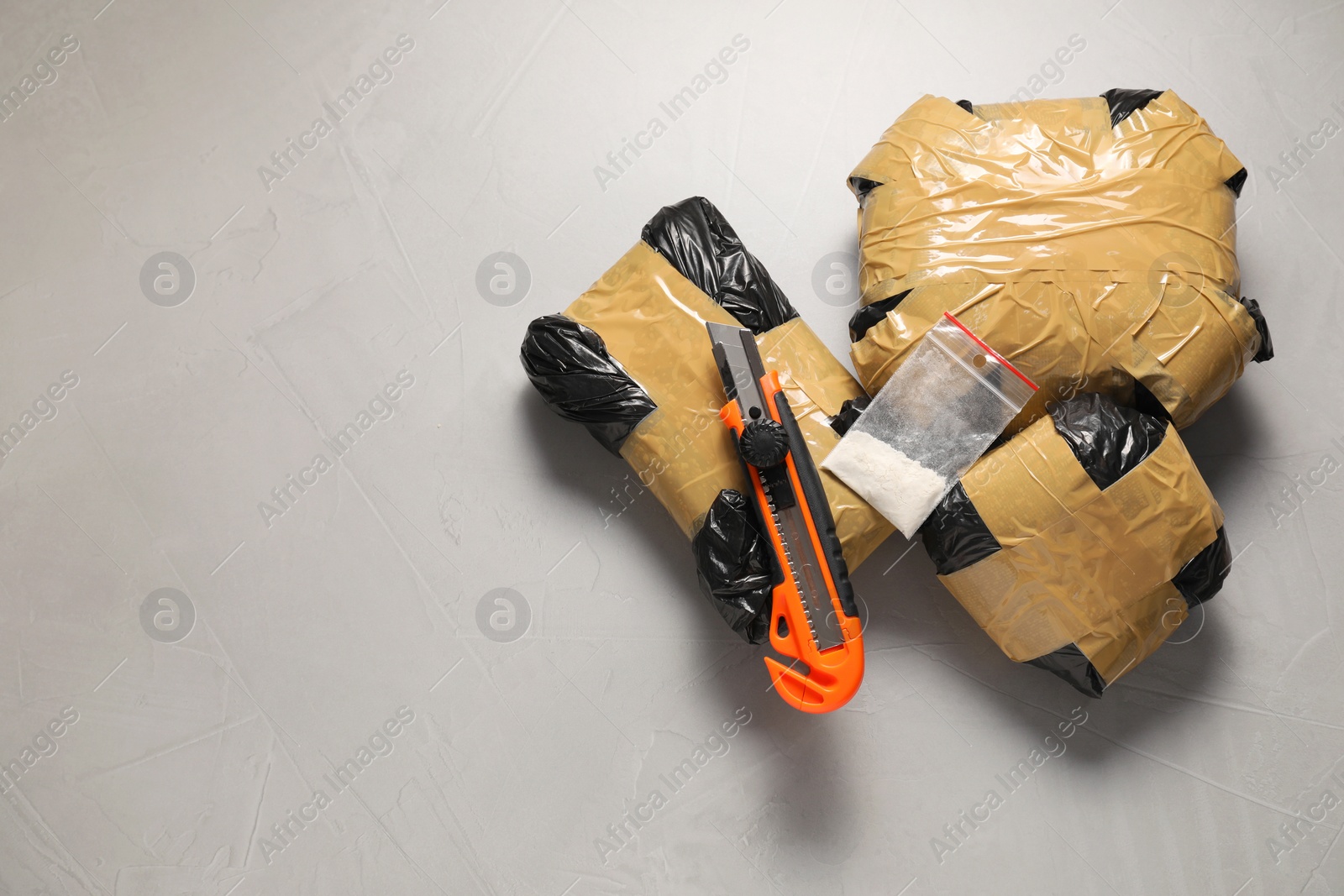 Photo of Packages with narcotics and stationery knife on grey textured table, flat lay. Space for text