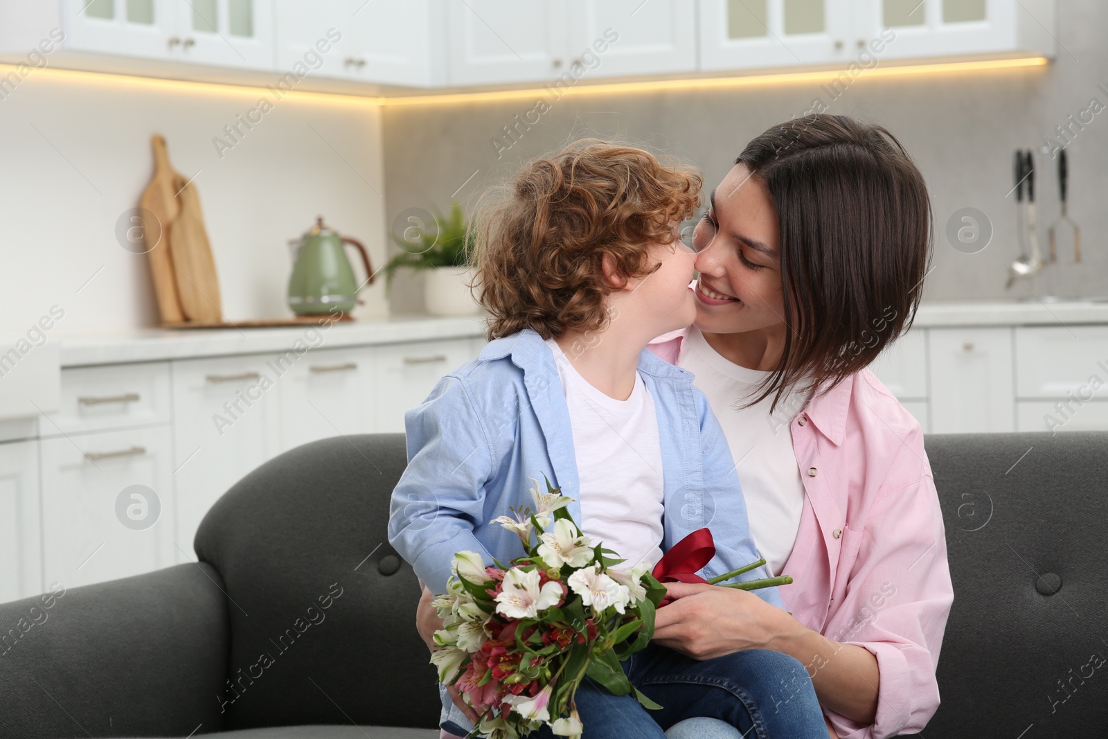 Photo of Happy woman with her cute son and bouquet of beautiful flowers at home. Mother's day celebration