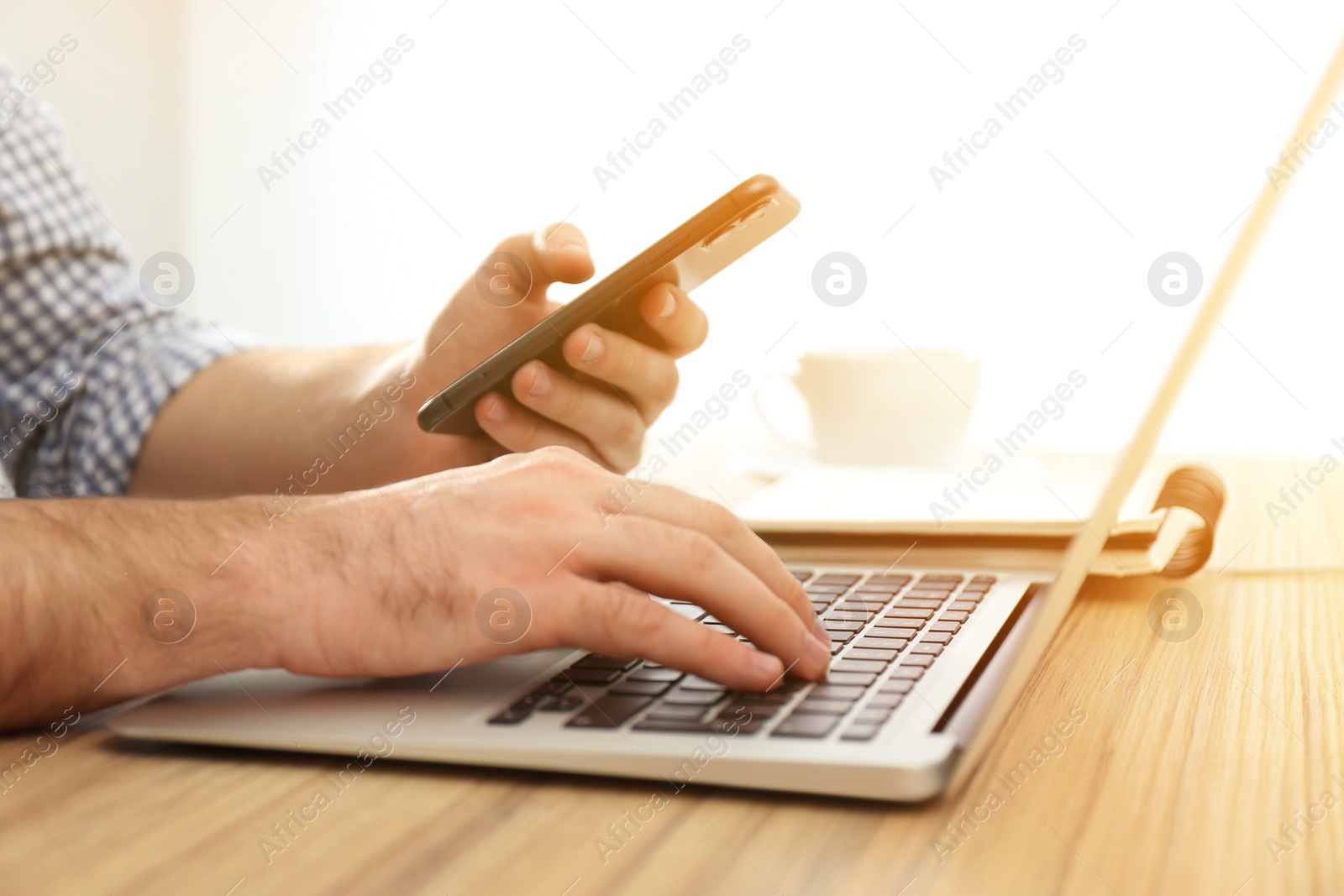 Image of Man with smartphone working on laptop at wooden table indoors, closeup