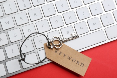 Keyboard, vintage key and tag with word KEYWORD on red background, top view