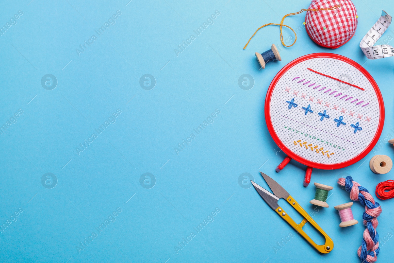 Photo of Flat lay composition with embroidery and different sewing accessories on light blue background. Space for text