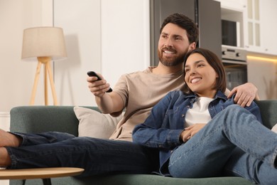 Photo of Happy couple watching TV on sofa at home