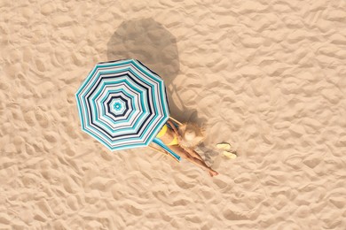 Woman resting in sunbed under striped beach umbrella at sandy coast, aerial view